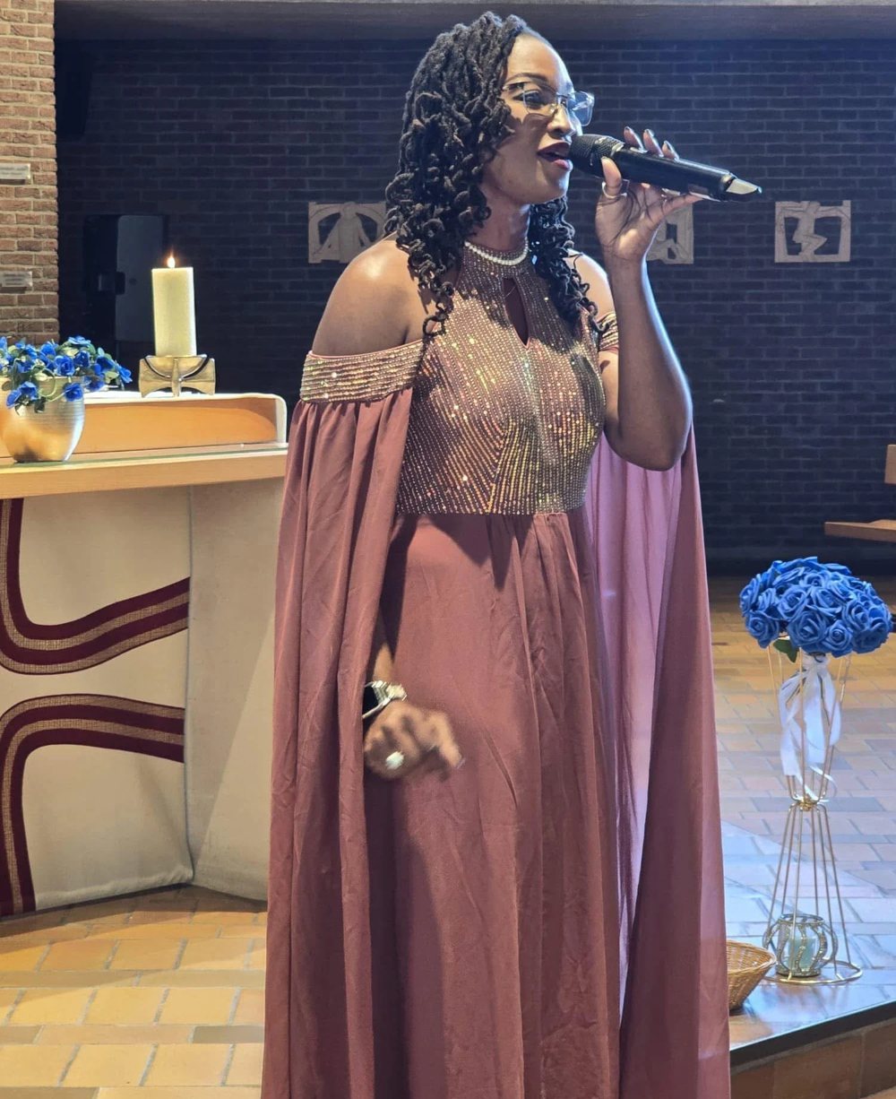 Buki singing in a mauve sequined gown with a sheer cape, a candle and blue flowers behind her